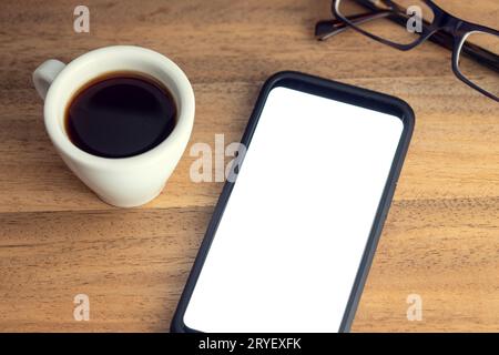 Téléphone intelligent sur bureau avec écran blanc, lunettes et une tasse de café sur table en bois. Modèle de maquette Banque D'Images