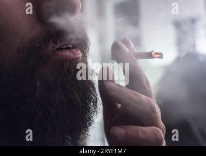 L'homme à la barbe fume une cigarette roulée Banque D'Images