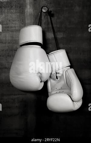 Gants de boxe en cuir blanc accrochés au mur noir Banque D'Images