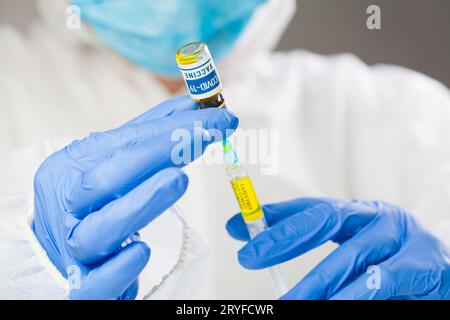 Médecin portant un masque facial protecteur, une combinaison et des gants tenant l'injection du vaccin contre le coronavirus Banque D'Images