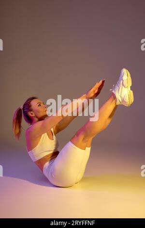 talentueuse sportswoman s'exerçant à étirer le corps faire des exercices de flexibilité en se penchant vers l'arrière, assis sur le sol s'adaptent à un mode de vie sain. isolé sur toute la longueur Banque D'Images