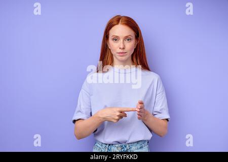 Photo de studio de jeune dame de gingembre gardant l'index sur la paume surélevée tout en montrant le numéro 100 sur la langue des signes, debout sur fond bleu Un deux-han Banque D'Images