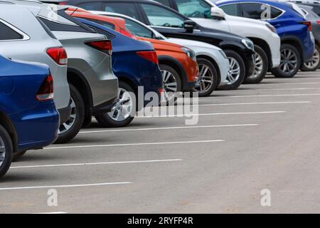 Rangée de voitures de couleur différente sur le parking asphalté à la journée nuageuse d'été Banque D'Images