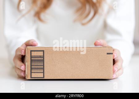 Femme en chemise blanche propre tenant dans les mains les marchandises livrées dans une boîte en carton. Modèle convivial avec espace de copie. Banque D'Images