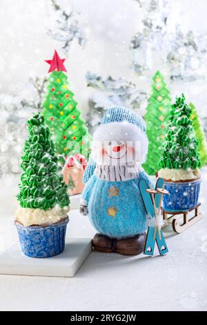 Carte avec un bonhomme de neige et cupcakes en forme de sapins de Noël. Banque D'Images