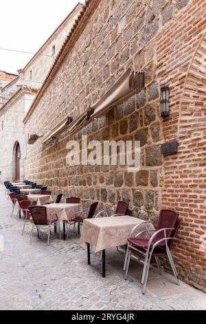 Petite rue médiévale pavée à Avila, Espagne, avec tables de restaurant et salle à manger, pas de gens. Banque D'Images