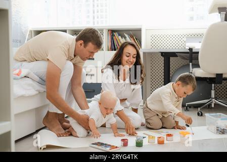 Parents avec deux enfants peignant sur le sol sur un gros rouleau de papier. Développer la créativité et l'imagination de l'enfant. Frères et sœurs utilisant des peintures pour dessiner ensemble Banque D'Images