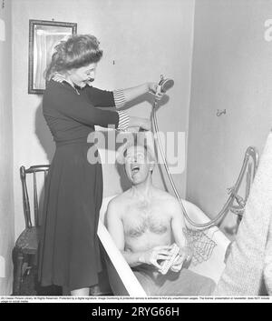 Couple dans la salle de bain dans les années 1940 Un homme est assis dans une baignoire avec seulement son pantalon. Une jeune femme rit et tient de manière ludique ses cheveux et la pomme de douche pour faire semblant de le doucher. Suède 1949. Kristoffersson réf. AT43-4 Banque D'Images