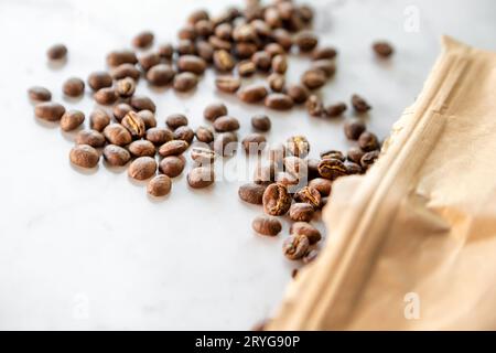 Grains de café torréfiés renversés du sac de papier sur la table en marbre, gros plan macro Banque D'Images