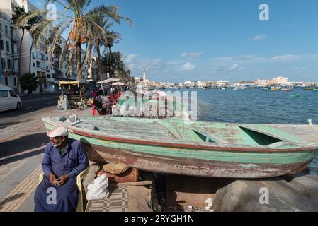 Un stand de souvenirs touristique informel à côté d'un bateau de pêche sur le front de mer méditerranéen de la deuxième plus grande ville d'Égypte, Alexandrie. Banque D'Images