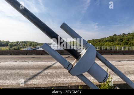 Gros plan de l'énorme ancre métallique en acier du câble de tension du pont haubané Lanaye, route rurale pour véhicules et canal Albert en arrière-plan, mauvais asphalte, s Banque D'Images