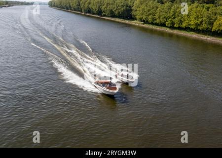 Deux petits bateaux naviguant à grande vitesse sur des eaux calmes le long du canal Albert, arbres verdoyants, fond flou et brumeux, journée d'été ensoleillée à Liège prov Banque D'Images