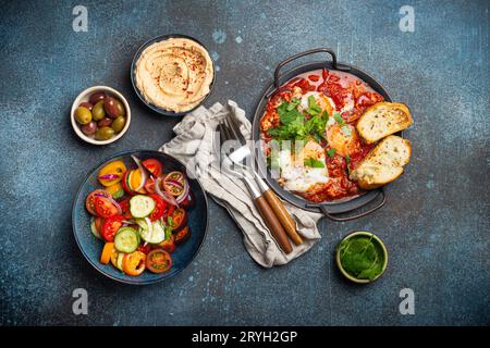 Petit-déjeuner ou brunch du Moyen-Orient avec Shakshouka dans une casserole, toasts, salade de légumes, houmous, olives Banque D'Images