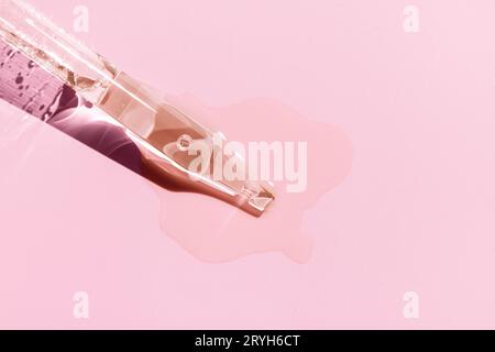 Gros plan d'une pipette avec du sérum liquide versé sur fond rose. Copier l'espace Banque D'Images