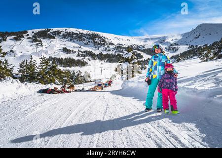 Mère et fille sur route enneigée, traîneau à chiens, montagnes et forêt en arrière-plan, Andorre Banque D'Images