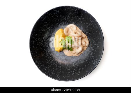 Anneaux de calmar en sauce avec purée de patates douces sur une assiette noire isolée. Photo de haute qualité Banque D'Images