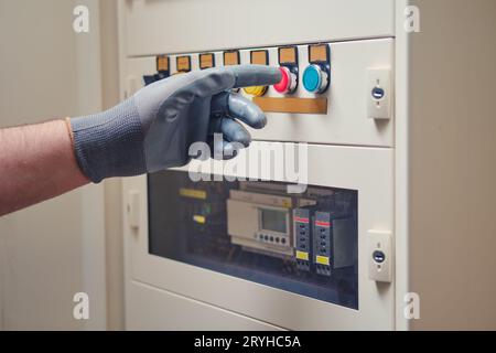 L'électricien inspecte les câbles à la recherche de signes de danger. En cas d'urgence, appuyez sur le bouton rouge de la carte de signalisation électrique. Banque D'Images