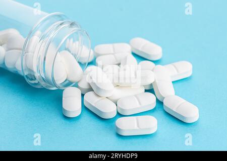 Pilules de médecine blanche renversant d'un récipient sur fond bleu Banque D'Images