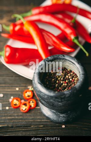 Mortier de marbre noir avec un pilon plein de grains de poivre mélangés avec des piments rouges sur fond Banque D'Images