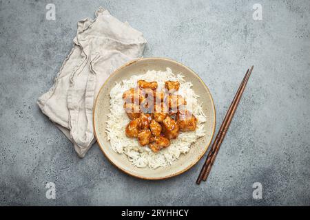 Poulet collant sucré et aigre chinois avec des graines de sésame et du riz sur une plaque en céramique avec des baguettes vue de dessus, pierre rustique grise ba Banque D'Images