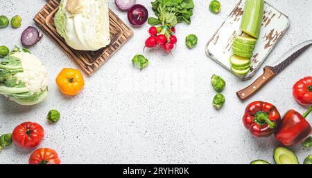 Légumes frais divers, planches à découper en bois et couteau sur table de cuisine blanche vue de dessus. Cuisiner un repas végétarien de sain Banque D'Images