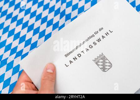 Augsbourg, Bavière, Allemagne - 29 septembre 2023 : enveloppe pour le vote postal pour les élections d'État en Bavière et le 8 octobre 2023 devant un drapeau bavarois. Enveloppe de vote *** Umschlag zur Briefwahl für die Landtagswahl in Bayern und Am 8 Oktober 2023 vor einer bayerischen Flagge. Stimmzettelumschlag Banque D'Images