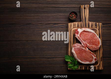 Couper les steaks de porc crus avec des assaisonnements sur la planche à découper de cuisine, vue de dessus de fond en bois rustique, prêt pour le barbecue. Longe de porc c Banque D'Images