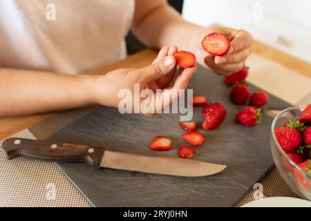 Gros plan de fraises fraîches coupées en tranches avec un couteau sur une planche dans la cuisine Banque D'Images