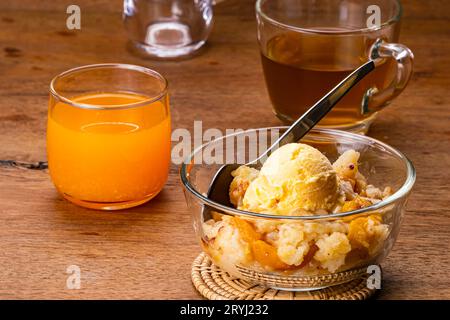 Vue à angle élevé de délicieux cordonnier de pêche maison avec une boule de crème glacée à la vanille et cuillère en métal dans un bol en verre transparent Banque D'Images