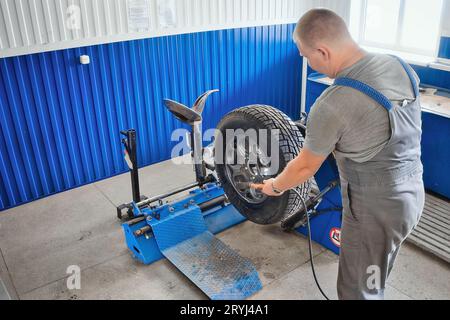 Le mécanicien automobile gonfle la roue de voiture avec le compresseur dans l'atelier de réparation de pneus. Le mécanicien change les pneus sur la roue, équilibre et gonfle le pneu. Service de voiture professionnel. Banque D'Images