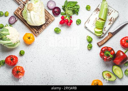 Légumes frais divers, planches à découper en bois et couteau sur table de cuisine blanche vue de dessus. Cuisiner un repas végétarien de sain Banque D'Images