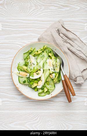 Saladier d'avocat vert sain avec œufs durs, concombres tranchés, haricots edamame, huile d'olive et herbes sur le dessus de la plaque en céramique vie Banque D'Images