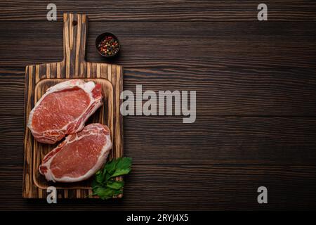 Couper les steaks de porc crus avec des assaisonnements sur la planche à découper de cuisine, vue de dessus de fond en bois rustique, prêt pour le barbecue. Longe de porc c Banque D'Images