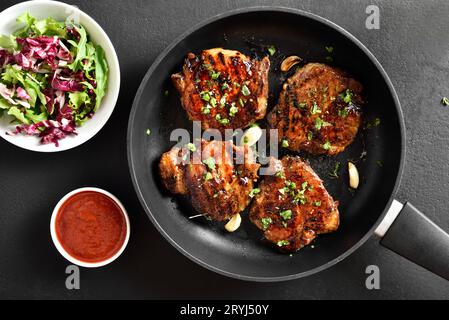 Steaks de porc rôtis dans une casserole sur fond de pierre noire. Vue de dessus, plan d'installation, gros plan Banque D'Images