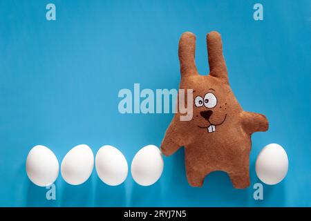 Chasse de Pâques avec lapin jouet et œufs de couleur dans le verre sur fond bleu Banque D'Images