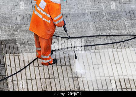 Travailleur nettoyant un trottoir de rue avec un jet d'eau à haute pression. Espace de copie Banque D'Images