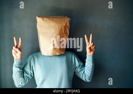 Homme positif heureux avec un sac en papier montrer le signe de victoire sur fond gris Banque D'Images