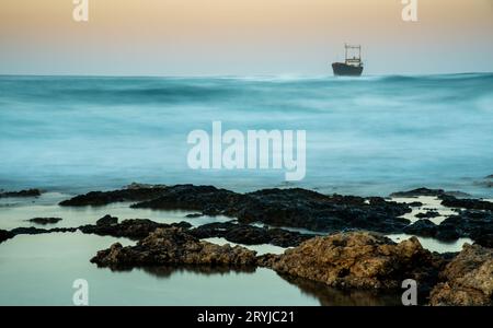 Bateau abandonné dans la mer orageux avec de grandes vagues de vent pendant le coucher du soleil Banque D'Images