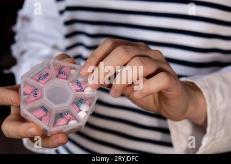 Femme trier les pilules Organiseur des injections hebdomadaires gros plan de la boîte de pilules médicales avec des doses de comprimés pour la journée prendre des médicaments avec des médicaments blancs roses et capsule Banque D'Images