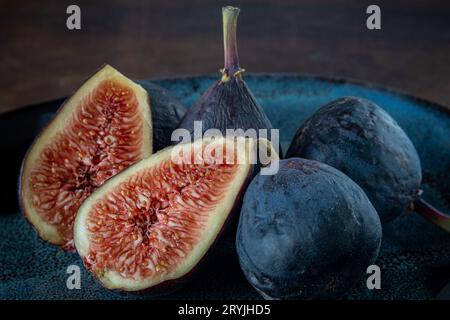 gros plan photo de figues aux fruits frais ; coupées et prêtes à servir, trois figues entières sur un fond sombre. Banque D'Images