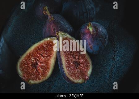gros plan photo de figues aux fruits frais ; coupées et prêtes à servir, trois figues entières sur un fond sombre. Banque D'Images