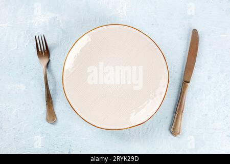 Une assiette blanche vide avec un bord doré, avec une fourchette et un couteau, au-dessus Banque D'Images