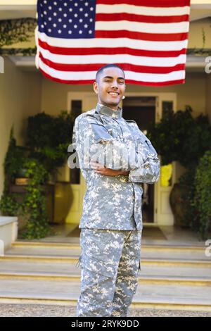 Portrait d'un homme biracial heureux soldat américain portant un uniforme militaire debout à l'extérieur de la maison Banque D'Images