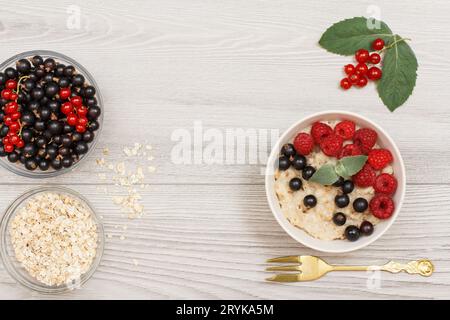 Bouillie d'avoine dans un bol en porcelaine avec baies de groseille et framboises, décorée de feuilles de menthe. Banque D'Images