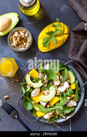 Salade diététique saine avec roquette, mangue, avocat, poulet grillé, noix et vinaigrette sur un comptoir en pierre sombre. Haut Banque D'Images