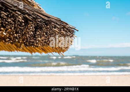 Parasol en rotin de plage de paille à la plage vide avec des fonds de ciel bleu mer côte océan. Journée de détente. Copiez l'espace pour votre texte. Banque D'Images