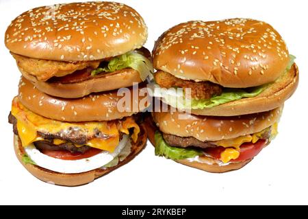 Pile de petits pains au sésame de patties de filet de poulet pané frit, laitue croustillante, tomates, fromage fondant, oignons et sauce, pâté de bœuf double épaisse et juteuse Banque D'Images