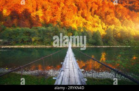 Pont en bois sur le lac dans les montagnes avec des arbres rouges au coucher du soleil Banque D'Images