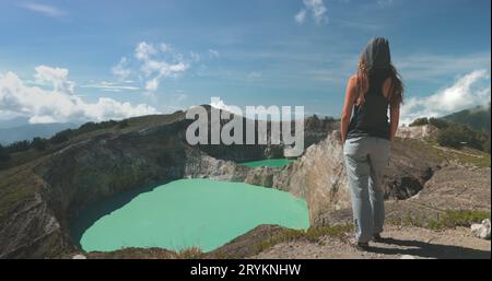 Femme touristique profiter de la vue matinale sur les lacs de cratère bleu volcanique Kelimutu. Arrière-plan de la nature. Destination du voyage. Beau paysage sauvage. Vacances d'été exotiques, randonnée, détente. Vue arrière rapprochée Banque D'Images