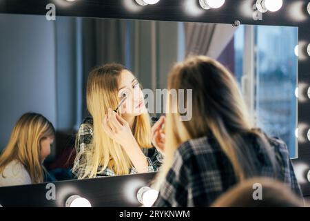 Jeune belle femme met la mascara sur les cils devant un grand miroir dans le dressing. Banque D'Images